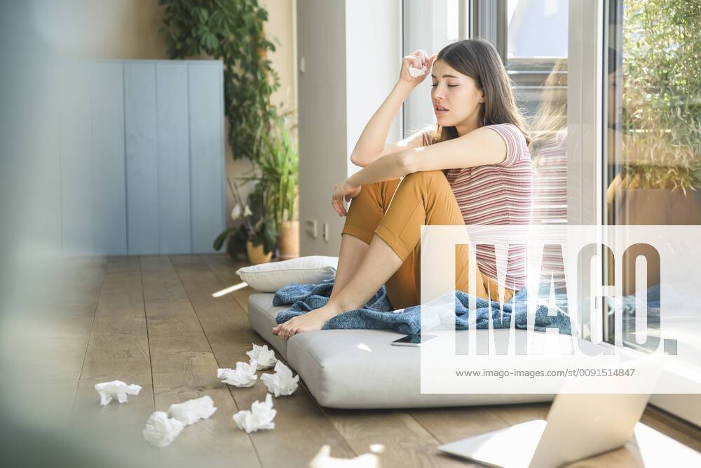 Sad young woman sitting at the window at home with laptop and tissues model released Symbolfoto property released UUF17008