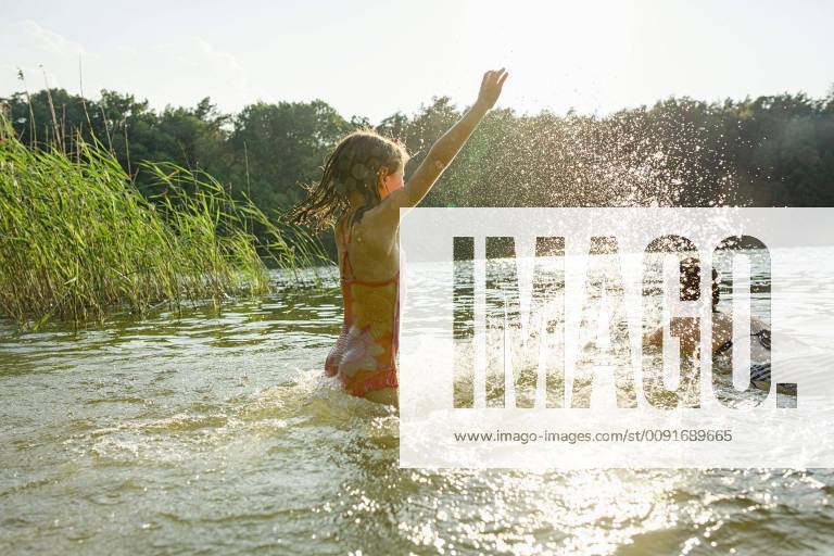 Playful girl splashing and woman swimming in sunny summer lake Germany Brandenburg