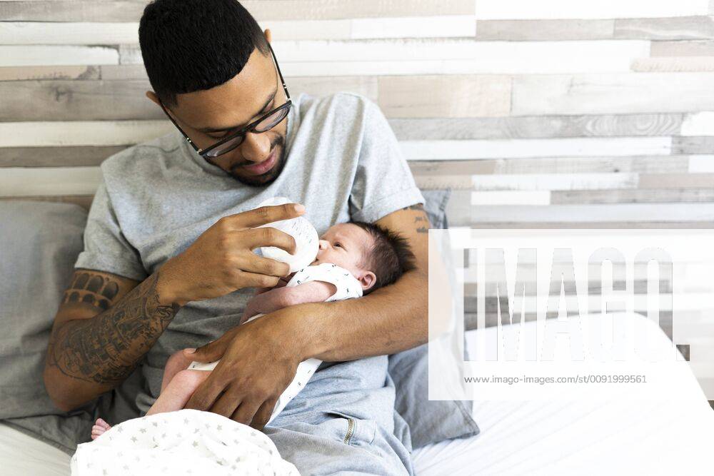 Father bottle-feeding his newborn baby in bed model released Symbolfoto property released ERRF01311