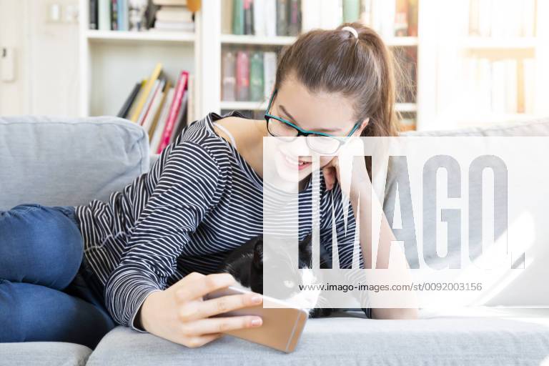Smiling girl lying on couch at home taking selfie with cat model released Symbolfoto property released LVF08006