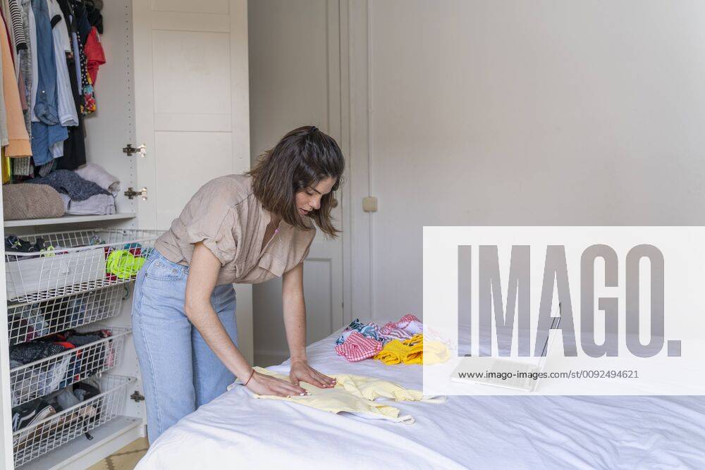 Young woman with laptop placing clothes on bed model released Symbolfoto AFVF03280