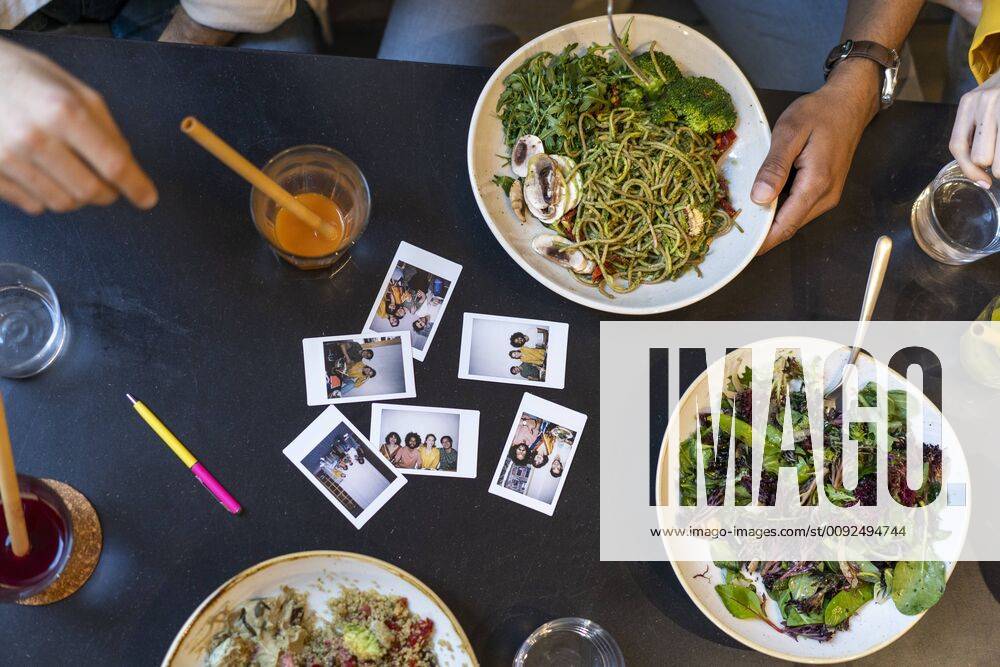 Group of friends having lunch in a restaurant with instant photos on table model released Symbolfoto property released AFVF03484