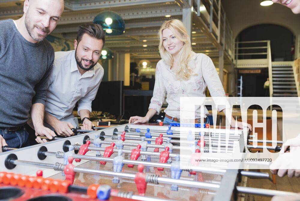 Happy colleagues playing foosball in office model released Symbolfoto property released FMOF00684