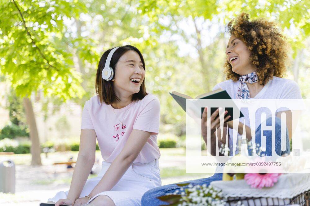 Two happy women with book and headphones relaxing in park model released Symbolfoto FMOF00719