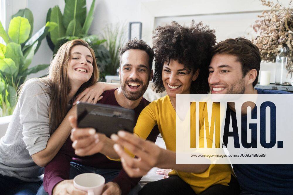 Four happy friends sitting on couch taking a selfie model released Symbolfoto property released GIOF06442