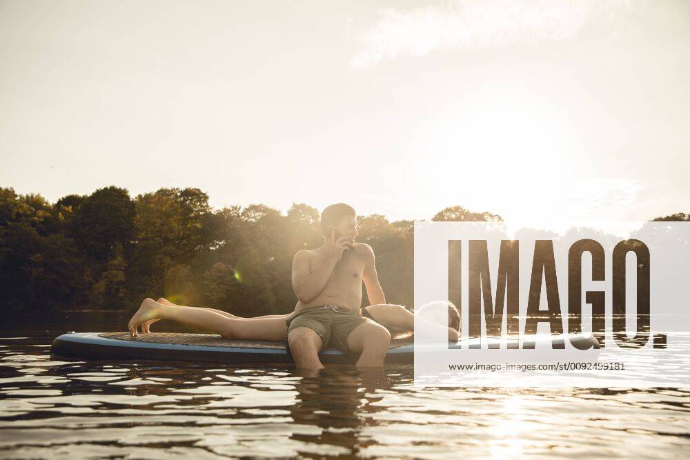 Youple on the lake, relaxing on a paddleboard, man talking on the phone model released Symbolfoto GUSF02349