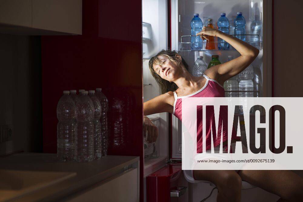 Woman refreshes herself sitting in front of the fridge ,model released, Symbolfoto