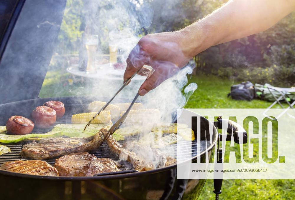 DEU, Deutschland, Münsingen, Baden-Württemberg, 24.08.2019: Grillfest im Garten. Auf dem Rost liegen Steaks vom Rind, Lammkeule, Schweinenacken sowie Tomaten, Mais und Zucchini.