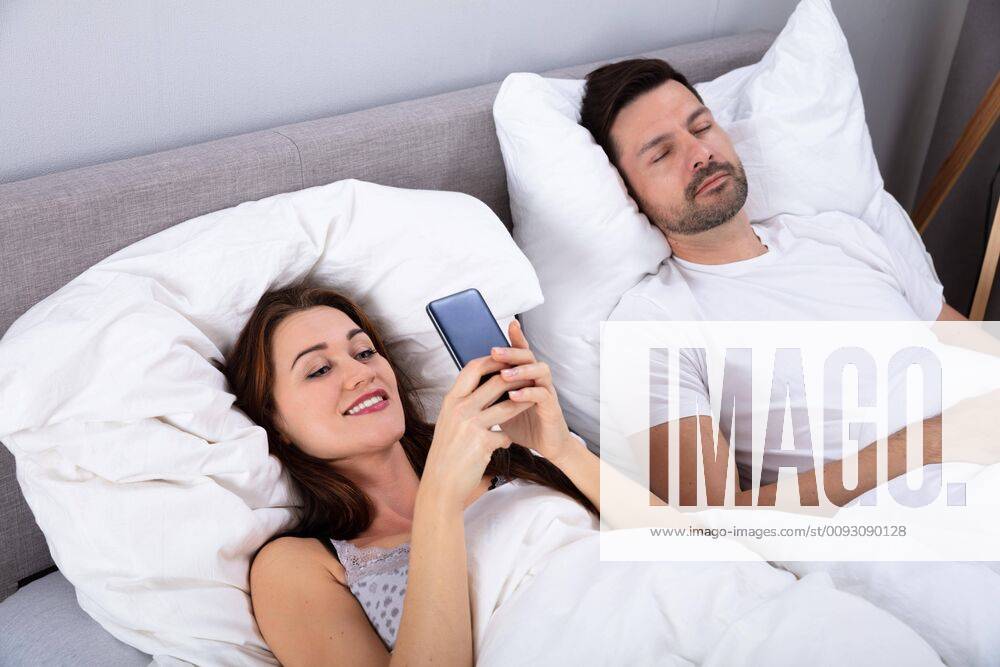 Woman Using Smartphone While Her Husband Sleeping On Bed ,model released, Symbolfoto