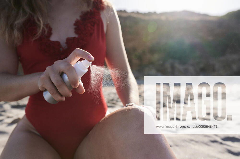 Young woman applying suncream spray on the beach model released Symbolfoto IGGF01319