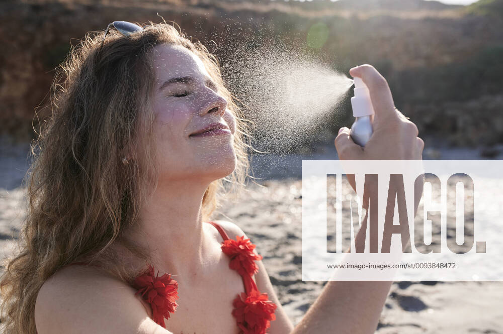 IMAGO Creative, Jahreszeit Sommer, Sonnenschutz Young woman applying suncream spray on the beach model released Symbolfoto IGGF01320