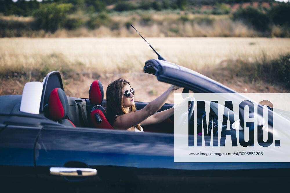 Young woman wearing sunglasses, sitting in her convertible model released Symbolfoto OCMF00604