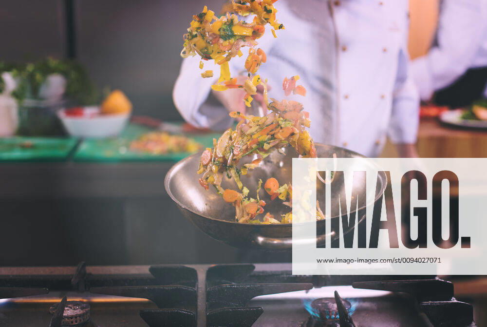 Young male chef flipping vegetables in wok at commercial kitchen. chef flipping vegetables in wok ING_32193_166532