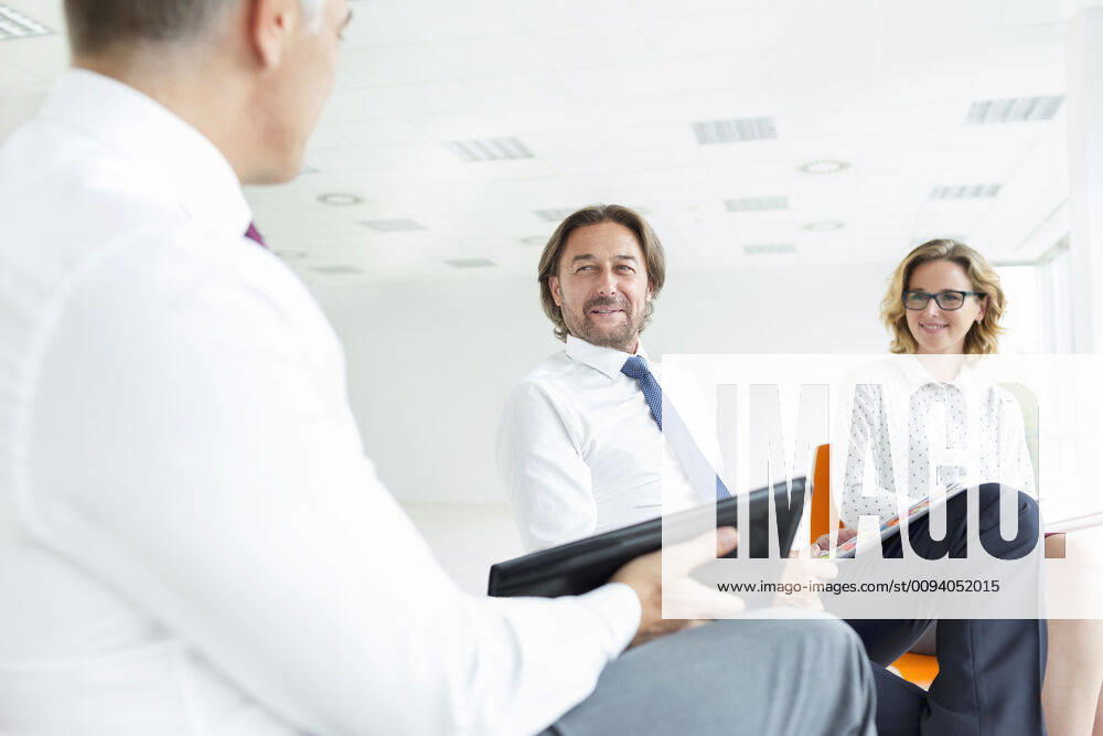 Smiling colleagues looking at businessman while sitting in new office during meeting,model released, Symbolfoto INH_19064_12277