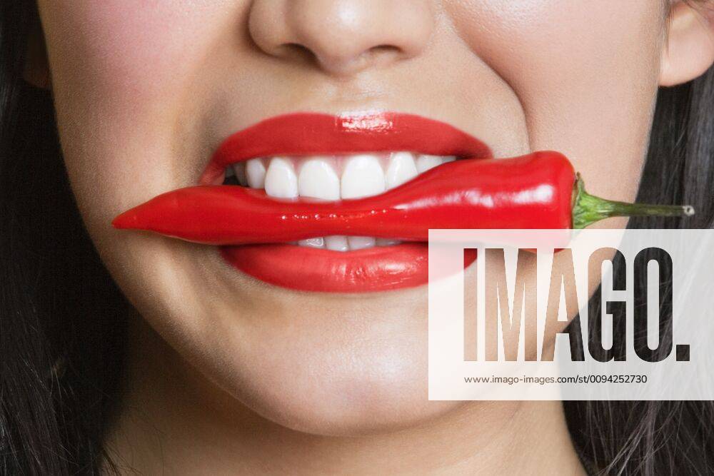 Close-up portrait of Hispanic woman biting red pepper,model released, Symbolfoto 03B96579
