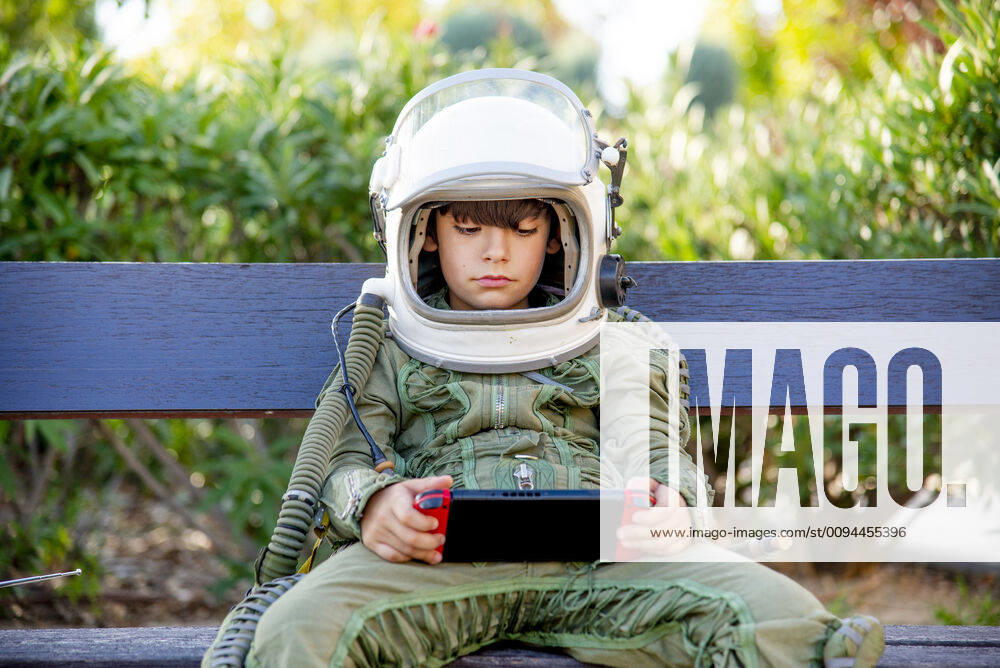 IMAGO Creative, Lifestyle, Gaming Boy wearing a space suit and sitting on a bench, playing alone with video games model released Symbolfoto CJMF00124
