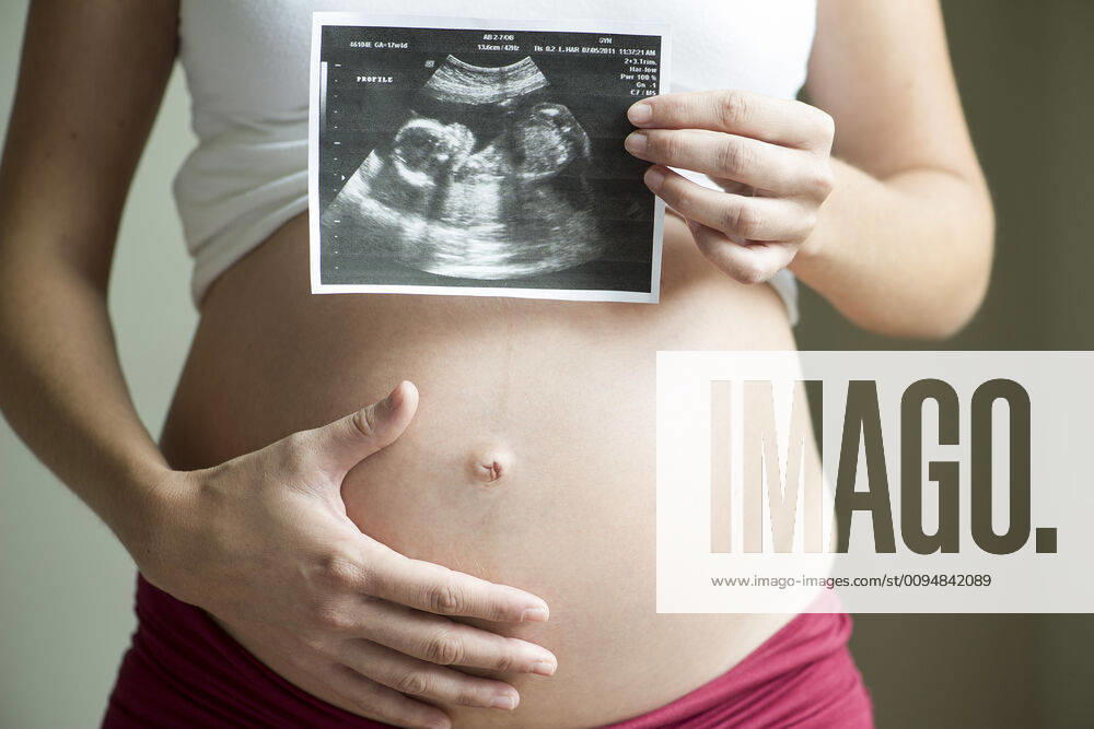 Pregnant woman holding ultrasound image, mid section