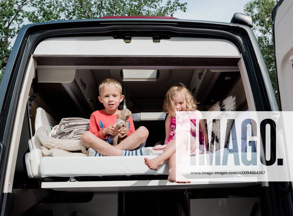 Brother and sister sat on a bed in a camper van on vacation in summer Sweden, Stockholm County, Norrtälje CR_RABE191011-182167-01