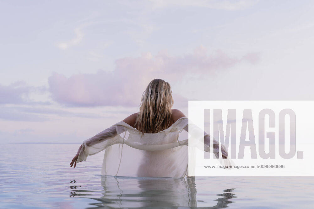 Rear view of young woman wearing white blouse inside sea during sunset model released Symbolfoto AFVF04353