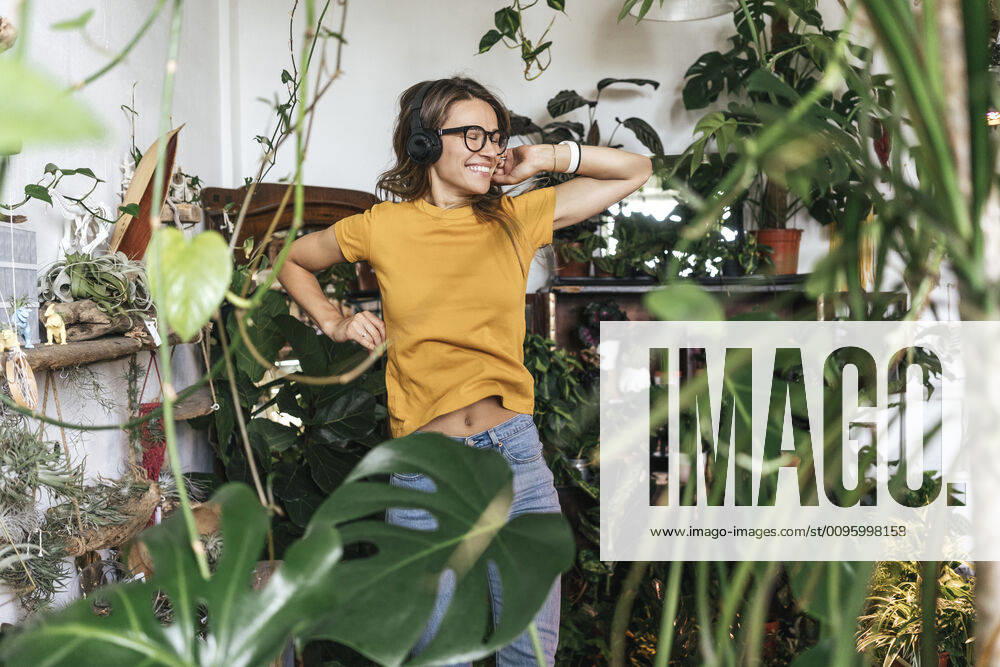 Cheerful young woman surrounded by plants listening to music with headphones model released Symbolfoto property released VPIF01877