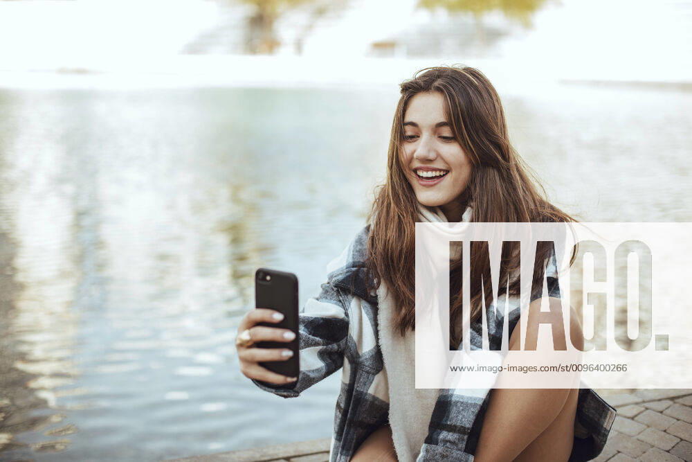Young brunette woman using smartphone and taking a selfie at lake model released Symbolfoto ACPF00659
