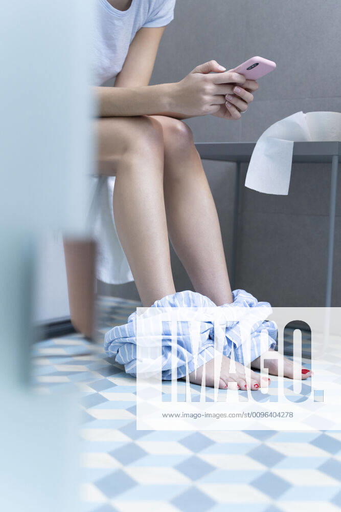 Young woman sitting on toilet and using smartphone model released Symbolfoto property released ERRF02555
