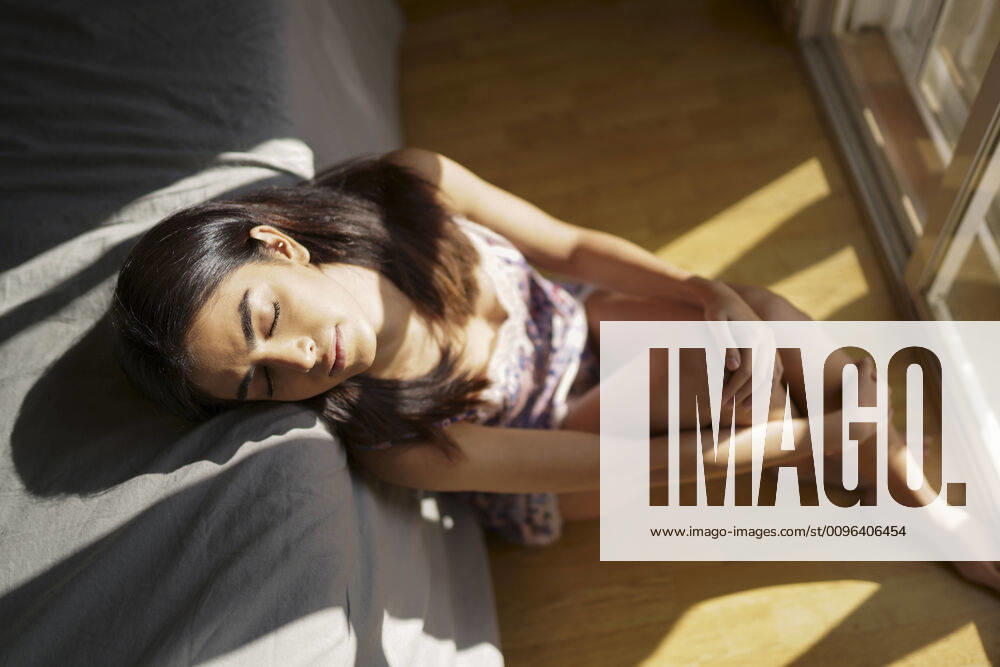 Portrait of young woman sitting on the floor of her bedroom enjoying sunlight in the morning model released Symbolfoto JSMF01430