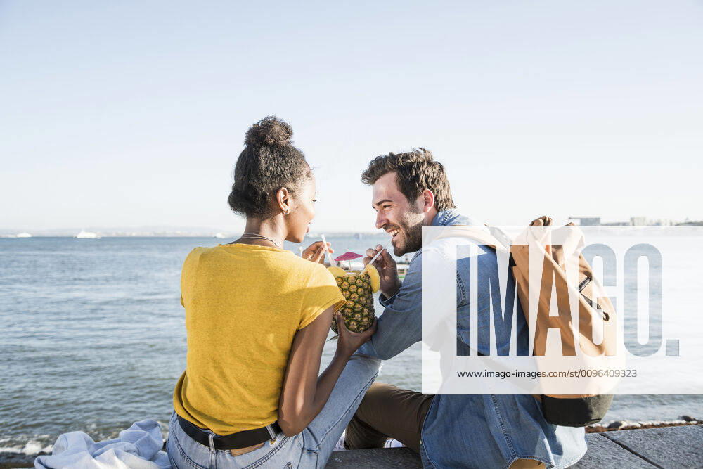 Happy young couple sitting at the waterfront sharing a drink in a pineapple, Lisbon, Portugal model released Symbolfoto UUF19847