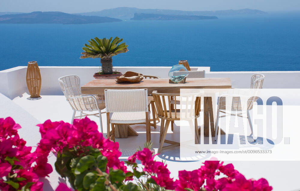 Furniture composed by a table and some chairs on a white floral terrace of a house in Santorini Greece where you can enjoy a meal while seeing a romantic seascape to the blue Aegean sea. Hori Oia, Greece CR_RUBO200106B-270556-01