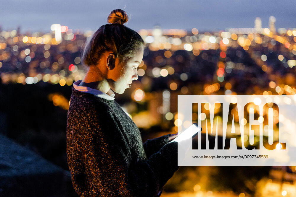 Young woman sitting on railing above the city using cell phone, Barcelona, Spain model released Symbolfoto GIOF07939