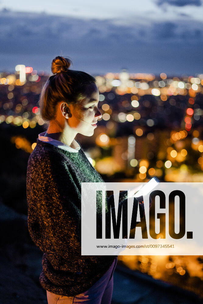 Young woman sitting on railing above the city using cell phone, Barcelona, Spain model released Symbolfoto GIOF07940