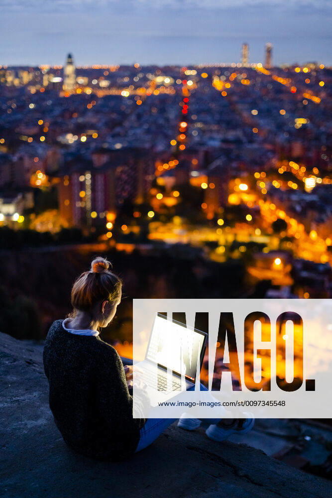 Young woman sitting on railing above the city using cell phone, Barcelona, Spain model released Symbolfoto GIOF07944