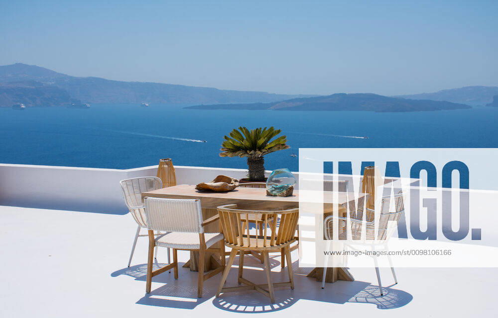 Furniture composed by a table and some chairs on a white terrace of a house in Santorini Greece where you can enjoy meal while seeing a romantic seascape to the blue Aegean sea. Horizontal ph Oia, Greece CR_RUBO200219-310702-01