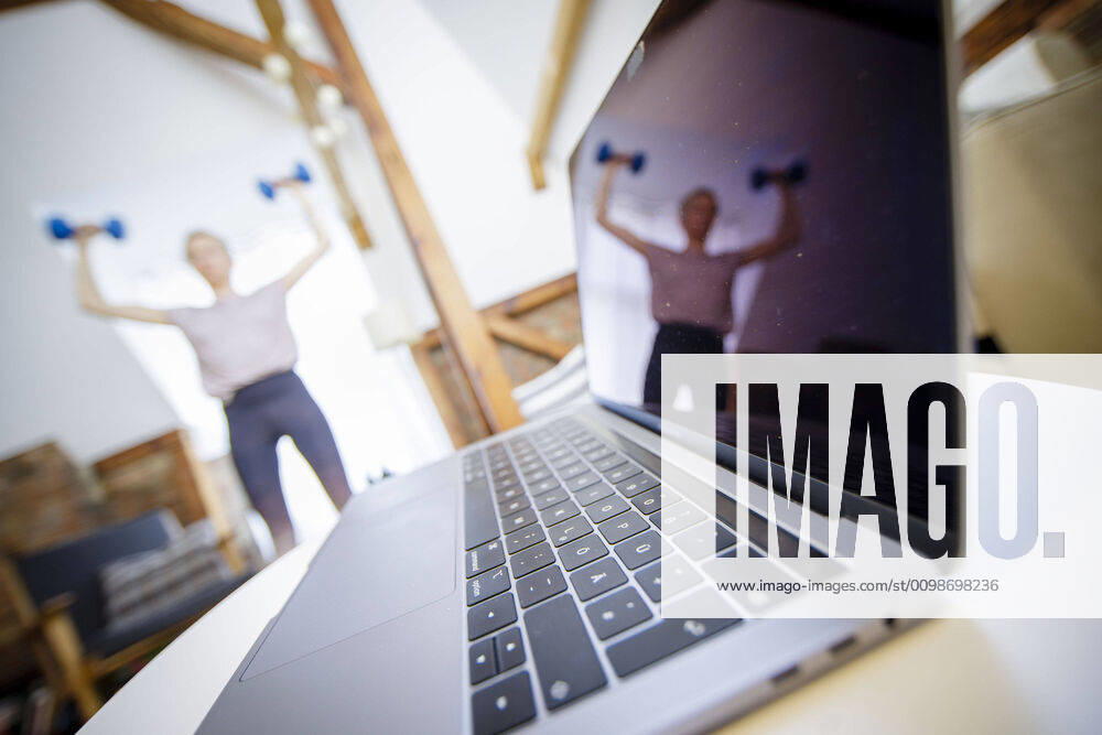 Symbolfoto zum Thema Fitness: Eine Frau trainiert zu Hause mit Hanteln. Neben ihr steht ein Laptop. Berlin, 26.03.2020. Berlin Deutschland