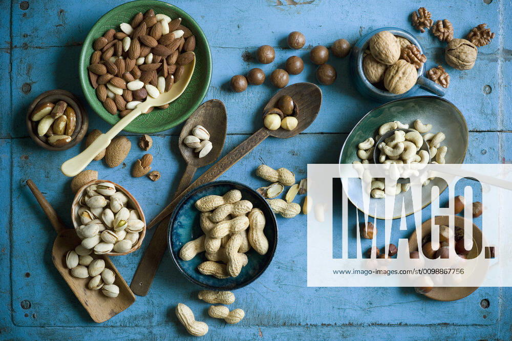 Overhead view of various nuts in bowls and on spoons on blue rustic table ASF06581