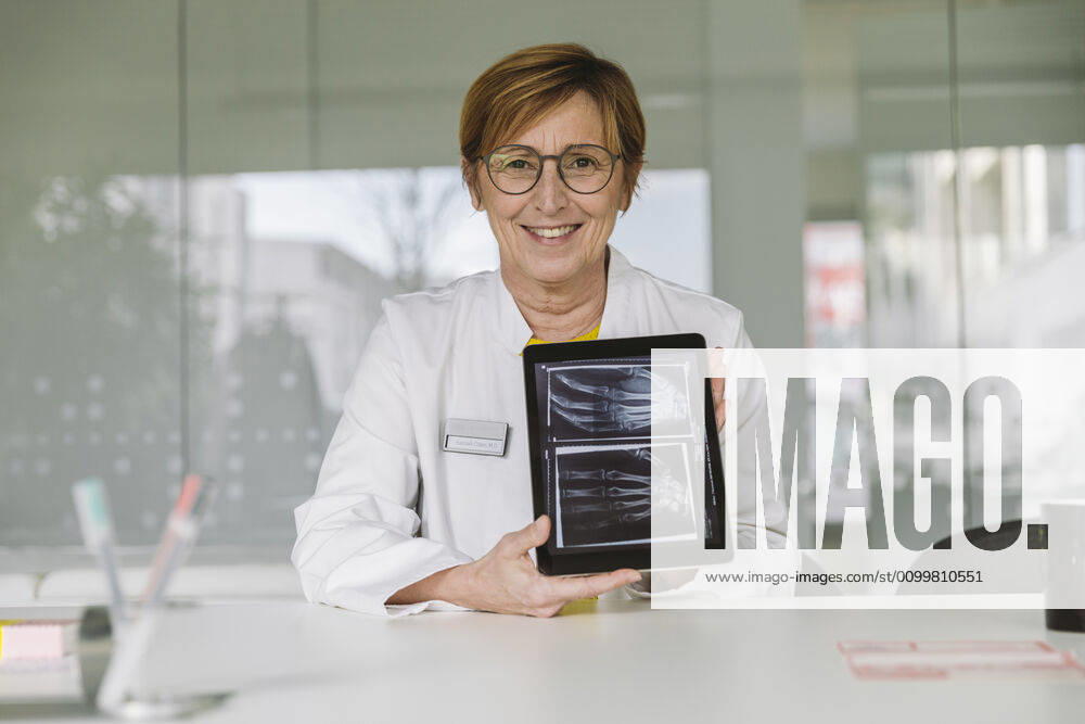 Doctor sitting at desk showing x-ray image of hand on digital tablet model released Symbolfoto property released MFF05499