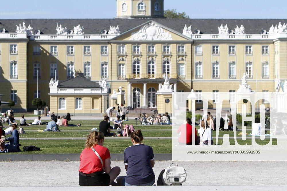 Personen sitzen unter Achtung der Abstandsregeln auf den Rasenflächen am Schlossplatz vor dem Landesmuseum und Schloss und genießen den warmen Frühlingstag in der Innenstadt von Karlsruhe, r Innenstadt von Karlsruhe, Baden Württemberg, Deutschland