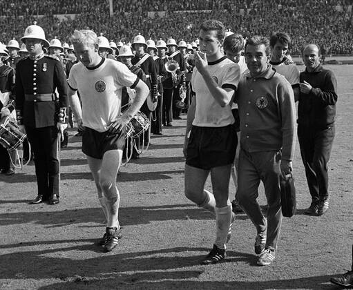 Fußball, WM 1966, Finale in Wembley, England - Deutschland 4-2 n.V. Mannschaftsarzt Hannes Schoberth (3.v.re.) und Co Trainer Dettmar Cramer (re.) führen nach der Niederlage die enttäuschten Karl Heinz Schnelliger (li.), Franz Beckenbauer (2.v.li.), Wolfgang Weber (dahinter)und Wolfgang Overath (alle BR Deutschland, 2. V. Fußball WM Herren Weltmeisterschaft 1966, Nationalmannschaft, Nationalteam, Nationaltrikot, Länderspiel, Finale, BRD Gruppe Musikkapelle, Orchester, Blasorchester, Karlheinz London, Blaskapelle, nachdenklich Enttäuschung, Nachdenklichkeit,