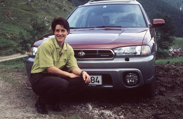 Uschi Disl mit Subaru Legacy in auto motor und tv (VOX) 09 98 böw Frau Weltmeisterschaft Biathlon dunkelhaarig kurzhaarig leger Shirt Hose Landschaft Gebirge Auto Wagen Kennzeichen kniend lächelnd ganz quer
