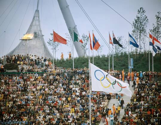 Eröffnungsfeier der Olympischen Spiele 1972 in München: Das Olympische Feuer brennt oberhalb der Zuschauer neben den Nationalfahnen der Teilnehmerländer
