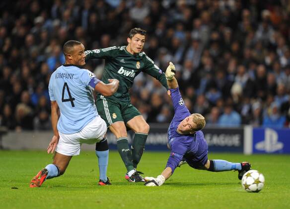 Cristiano Ronaldo of Real Madrid gets his shot away between Vincent Kompany of Manchester City and Joe Hart of Manchester City - UEFA Champions League Group D - Manchester City vs Real Madrid - Etihad Stadium - Manchester - 21 11 12 - EDITORIAL USE ONLY. No use with unauthorised audio, video, data, fixture lists, club league logos or live services. Online in-match use limited to 120 images, no video emulation. No use in betting, games or single club league player publications.