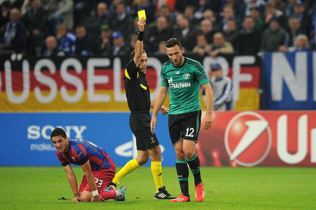 Fußball Champions League Gruppenphase 1. Spieltag Schalke 04 - Steaua Bukarest am 18.09.2013 in der Veltins Arena in Gelsenkirchen FIFA-Schiedsrichter Cüneyt Cakir ( Türkei ), hinten - zeigt Marco Höger ( Schalke ), rechts die gelbe Karte - Nicolae Stanciu ( Bukarest ), links am Boden