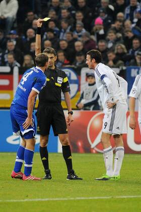 Der verletzte Benedikt Hoewedes ( links Schalke 04 ) bekommt von Schiedsrichter Paolo Tagliavento ( mitte ) die gelbe Karte gezeigt. 11.12.2013 --- Fussball --- Champions League --- Schalke 04 vs FC Basel Foto: Eibner EP_TTL