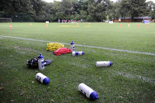 VDV-Trainingscamp --- Fussball --- 1.Bundesliga --- 09.07.2012 Flaschen, Schuhe und Leibchen der VDV, im Hintergrund die Mannschaft beim Training, allgemein, Feature, Hintergrund, Hinterleger