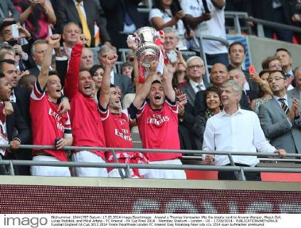 Arsenal s Thomas Vermaelen lifts the trophy next to Arsene Wenger, Mesut Özil, Lukas Podolski, and Mikel Arteta - FC Arsenal - FA Cup Final 2014 - Wembley Stadium - London - UK - 17 05 2014 - EDITORIAL USE ONLY. No use with unauthorised audio, video, data, fixture lists, club league logos or live services. Online in-match use limited to 120 images, no video emulation. No use in betting, games or single club league player publications.