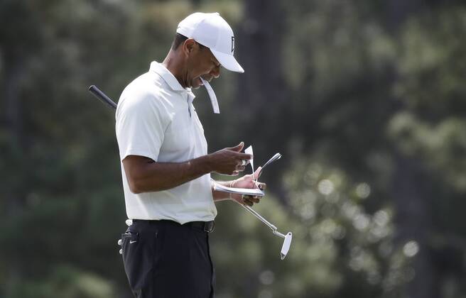 Tiger Woods holds a paper in his mouth on the first hole green in the 2nd round of the 2018 Masters Tournament at the Augusta National Golf Club in Augusta, Georgia, on April 6, 2018.  AUG20180406129 JOHNxANGELILLO