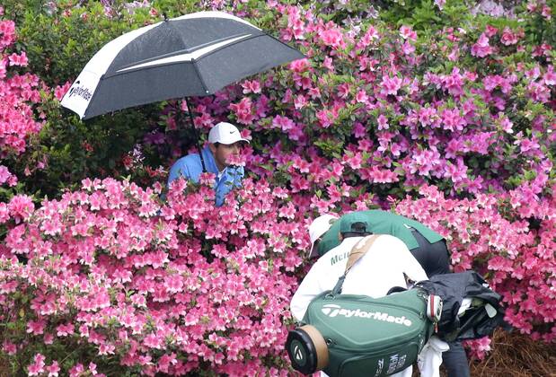 Bilder des Tages - SPORT Rory McIlroy of Northern Ireland holds an umbrella standing in a pack of azalea plants while caddie Harry Diamond and a referee identify his golf ball near the 13th green in the 3rd round of the 2018 Masters Tournament at the Augusta National Golf Club in Augusta, Georgia, on April 7, 2018.  AUG20180407121 JOHNxANGELILLO