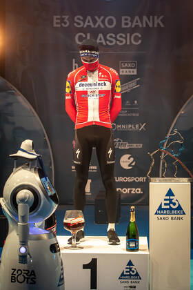 Radsport, E3 Harelbeke - Roboter führt Siegerehrung durch Kasper Asgreen (DEN DK - Deceuninck-Quick Step) bei der Siegerehrung - hier bei der Siegerzeremonie mit eigenstaendiger Uebernahme der Medaille von einem ferngesteuerten Roboter der die Ehrendamen Podiumsdamen Hostessen wegen der Covid-19 Corona Pandemie und der angemahnten Kontaktbeschraenkungen ersetzt - hier abgeschottet in der Sporthalle von Harelbeke ohne Zuschauer wegen der Covid-19 Corona Pandemie - Podium - Siegerehrung - Ehrung - Auszeichnung - Zeremonie - Zelebrierung - Ceremony - Jubel - Freude - Luck - Emotion - Emotionen - Mimik - Mimic - Gestik - Gestic - Hochformat hoch hochkant vertikal Event Veranstaltung: 64. E3 Saxo Bank Classic - Harelbeke nach to Harelbeke 203.9 km - Ort Location: Harelbeke - Region: West-Vlaanderen (Flandern) - Land Country: Belgien Belgium - Datum Date: 26.03.2021