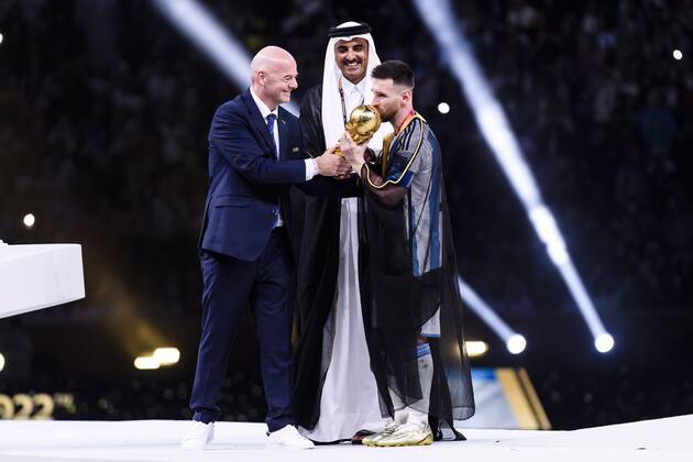 18.12.2022, Fussball Weltmeisterschaft 2022 in Katar, Finale, Argentinien - Frankreich, im Lusail Iconic Stadium (Lusail). Nach dem Gewinn des Finales küsst Weltmeister Lionel Messi (Argentinien) den WM-Pokal, eingehüllt in einen traditionellen arabischen Bisht, zuvor überreicht vom Emir, li: FIFA-Präsident Gianni Infantino und Katar Emir Tamim bin Hamad Al Thani (re) reichen dem Weltmeister den WM-Pokal.