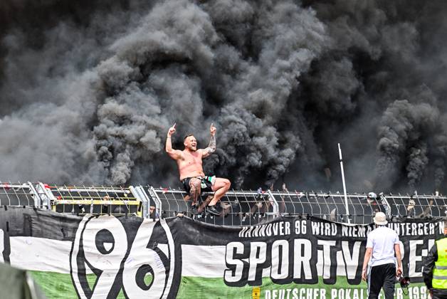 Bilder des Jahres 2025, Sport 05 Mai Sport Themen der Woche KW18 Sport Bilder des Tages GER, 2. BL, SSV Ulm 1846 vs Hannover 96 03.05.2025, Donaustadion, Ulm, GER, 2. BL, SSV Ulm 1846 vs Hannover 96, im Bild Ultra aus Hannover sitzt auf dem Zaun, dahinter ziehen Rauchschwaden von Pyrotechnik und Bengalos